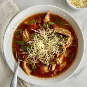 A bowl of cooked Chicken Minestrone Soup topped with parmesan cheese.