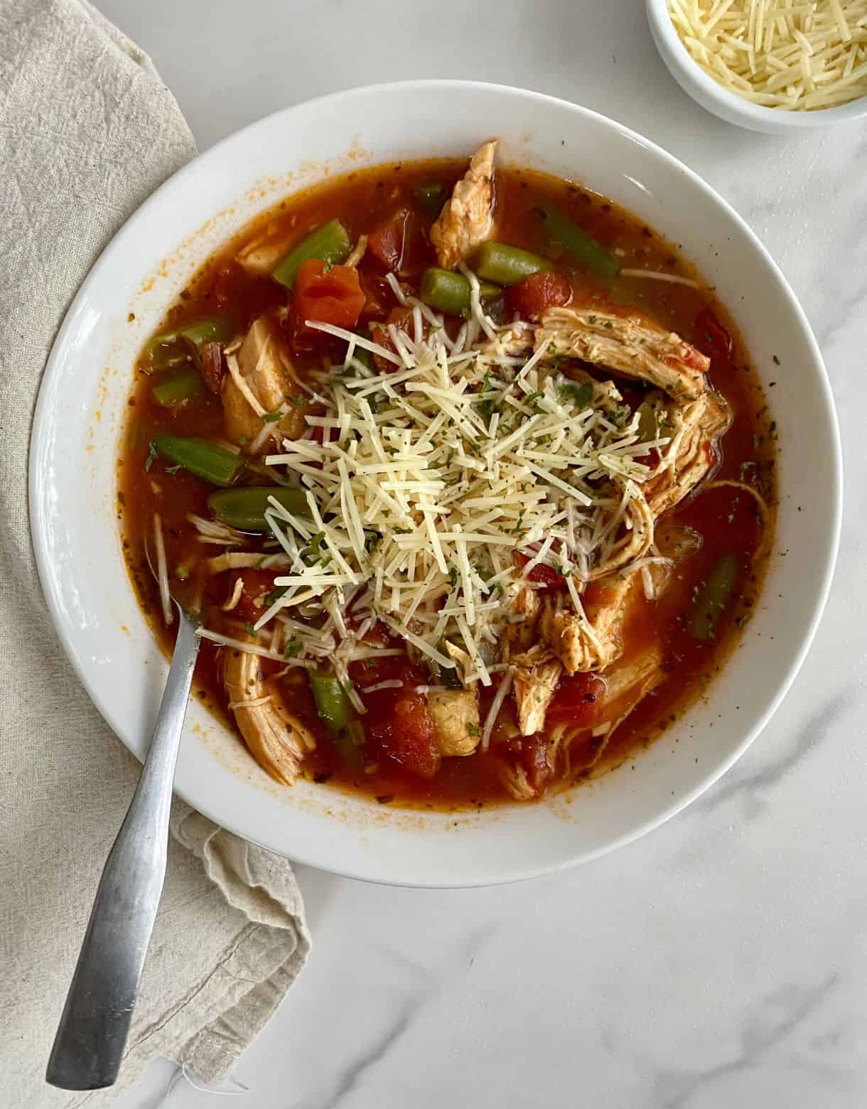 A bowl of cooked Chicken Minestrone Soup topped with parmesan cheese.