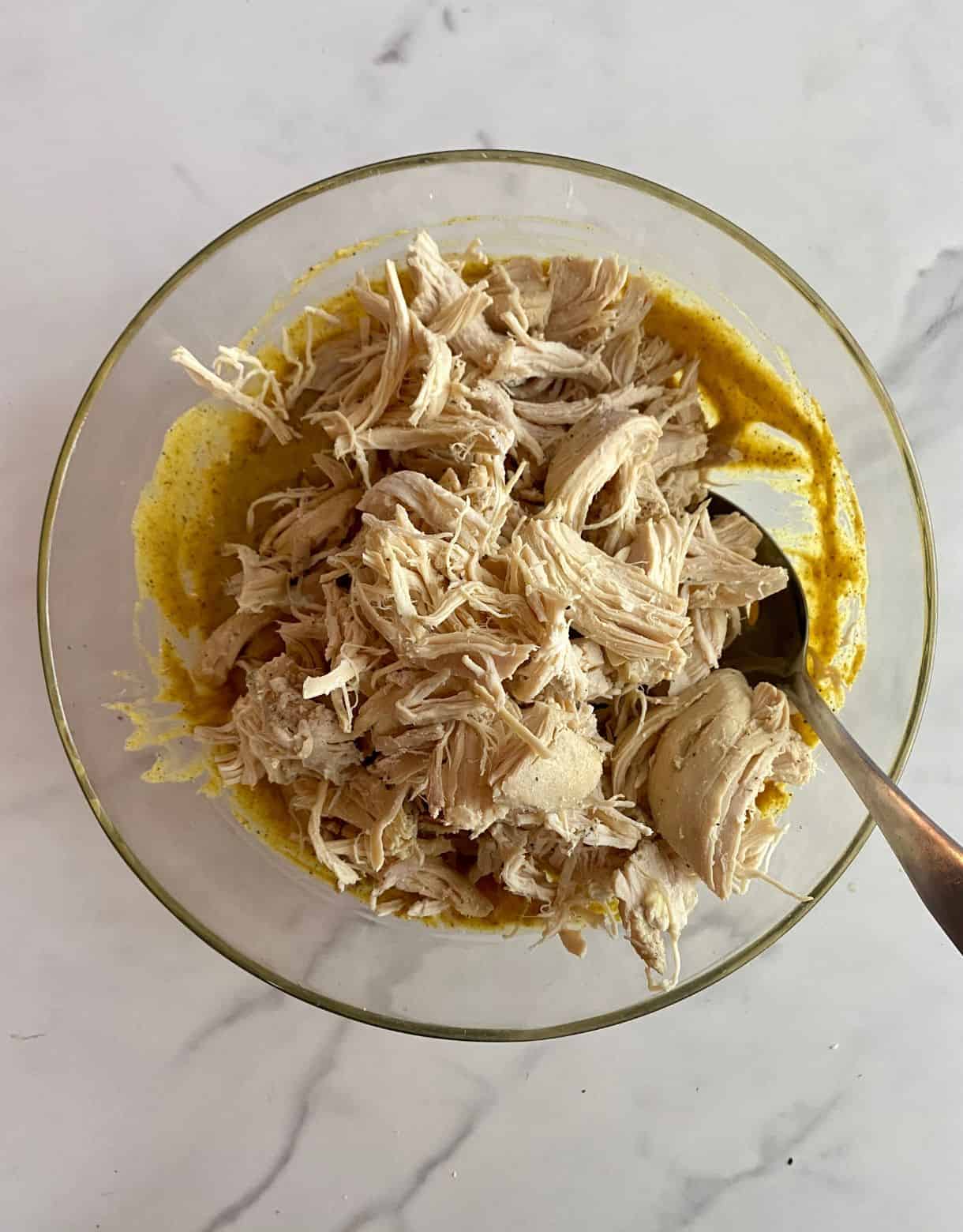 A bowl of curry dressing with shredded chicken added but not yet stirred.