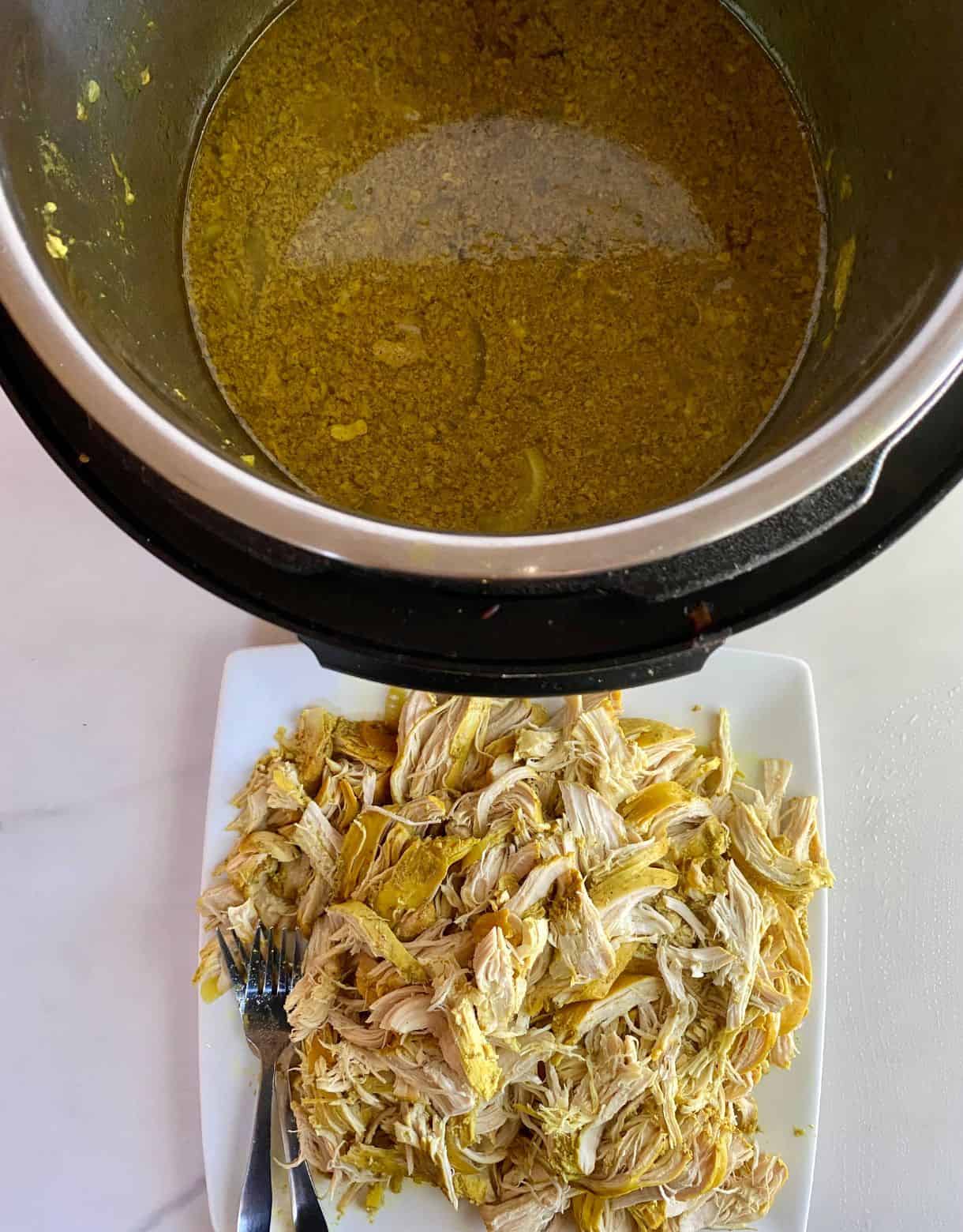 A plate of shredded curry chicken and a slow cooker with the cooking juices.