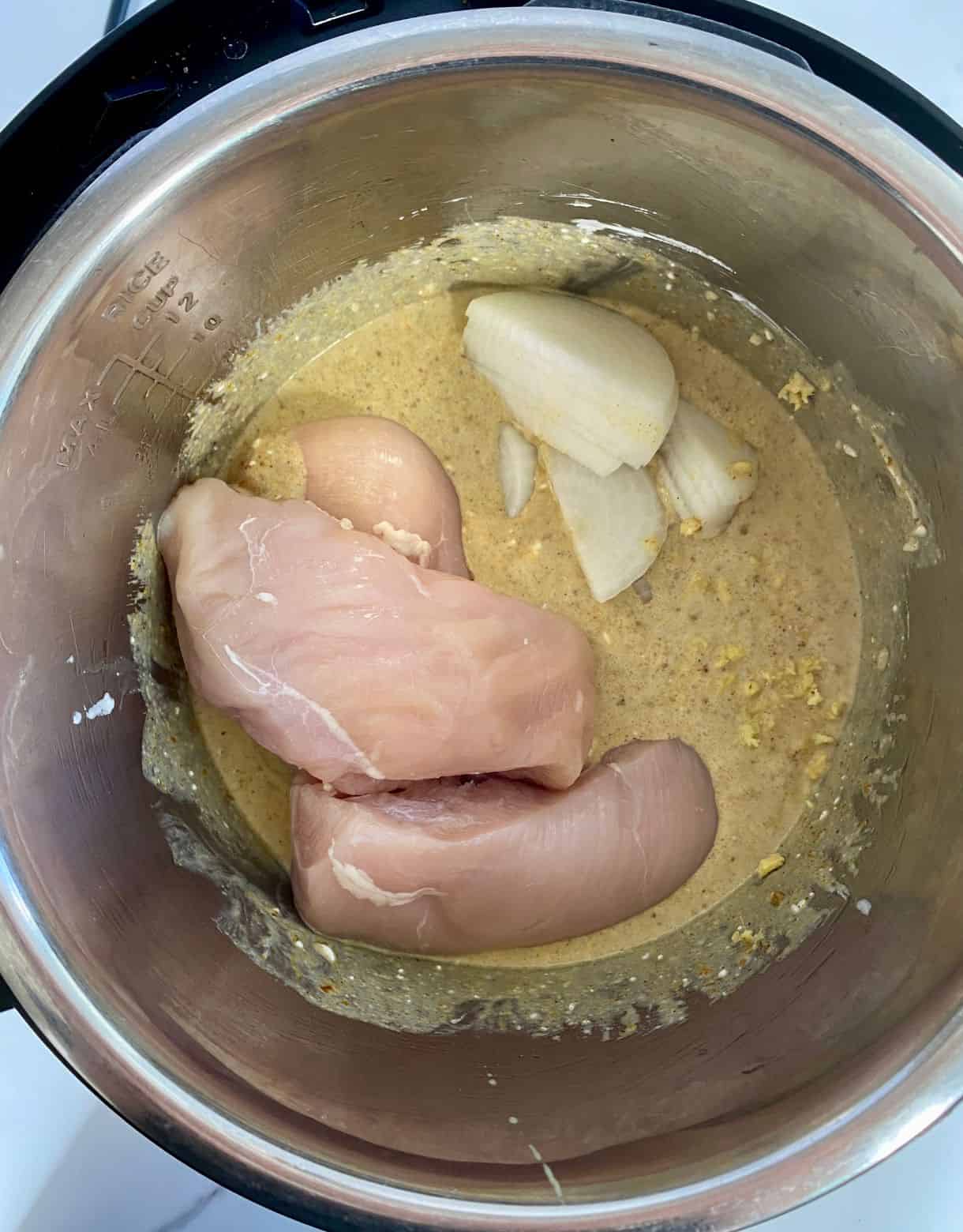 A slow cooker with the ingredients added for curry chicken but not yet stirred or cooked.