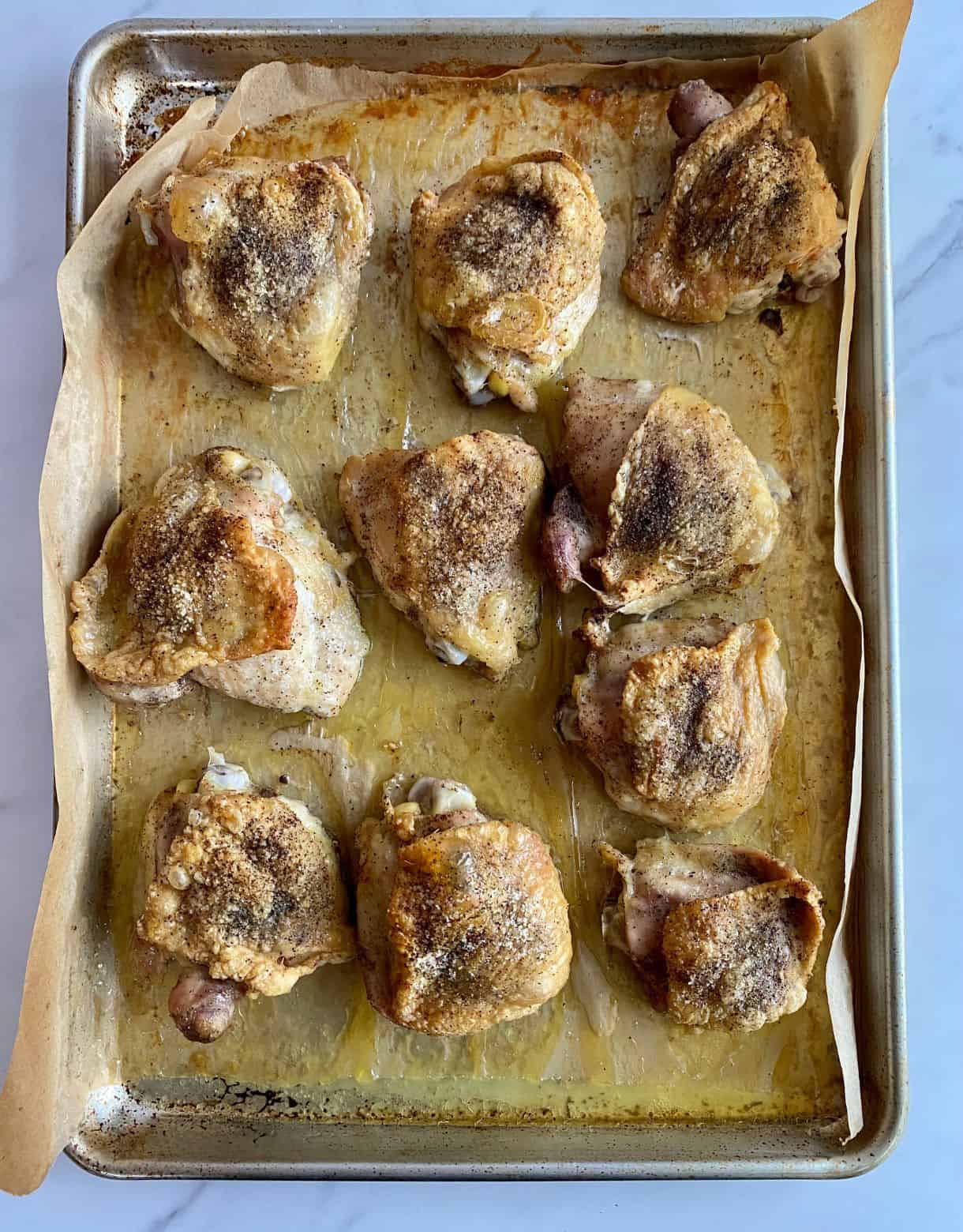 A sheet pan lined with parchment paper with cooked chicken thighs.