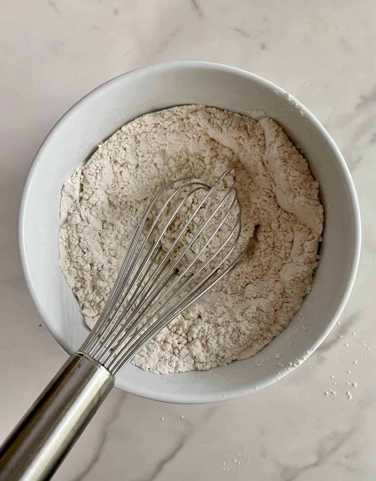 A bowl with flour, salt and baking soda and a whisk.