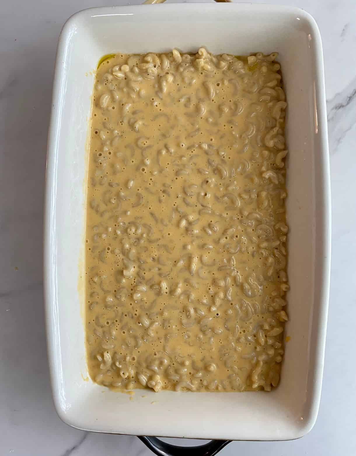 A casserole dish with mac and cheese spread into it but not yet baked.