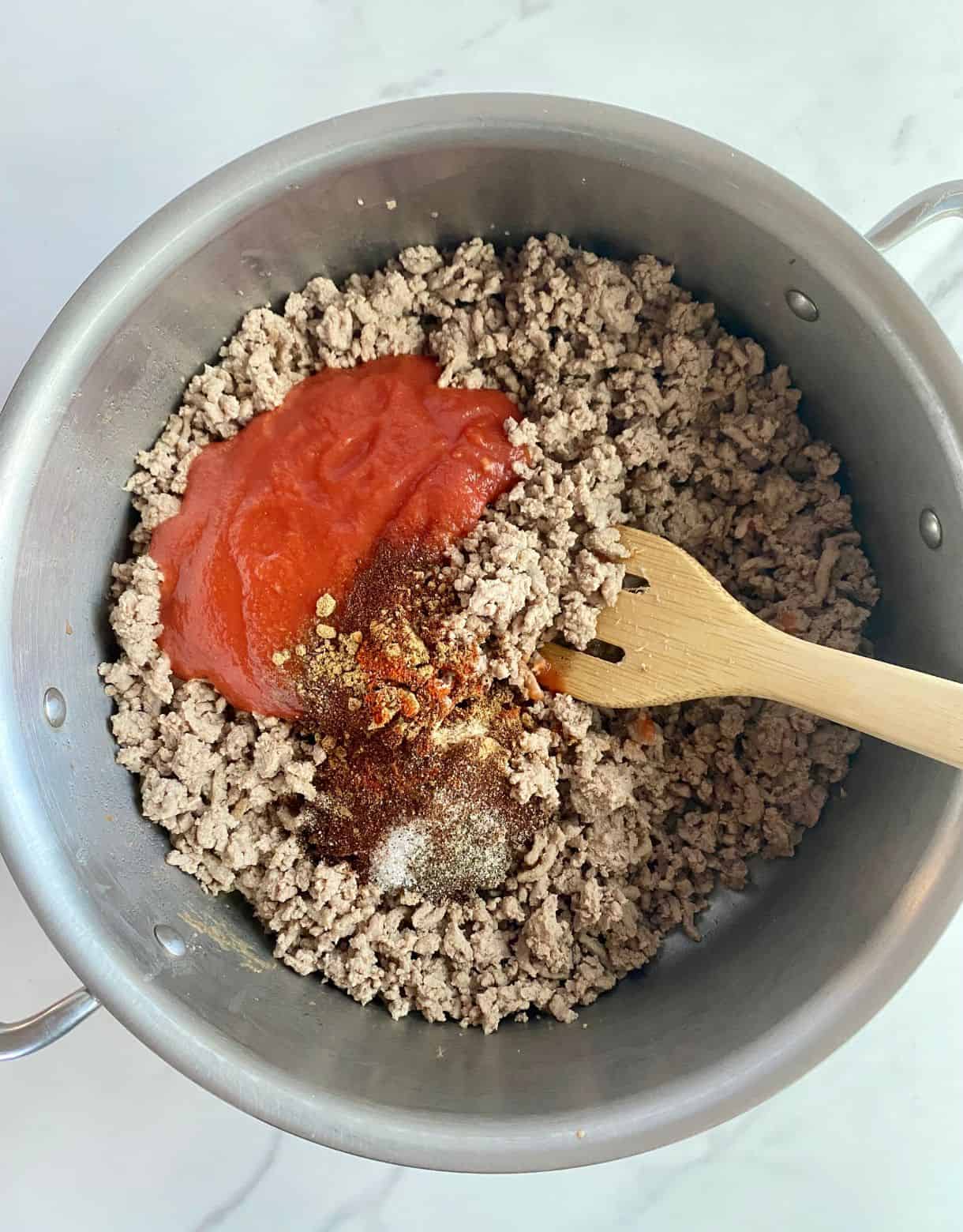 A skillet with cooked ground turkey and tomato sauce and spices added but not yet stirred.