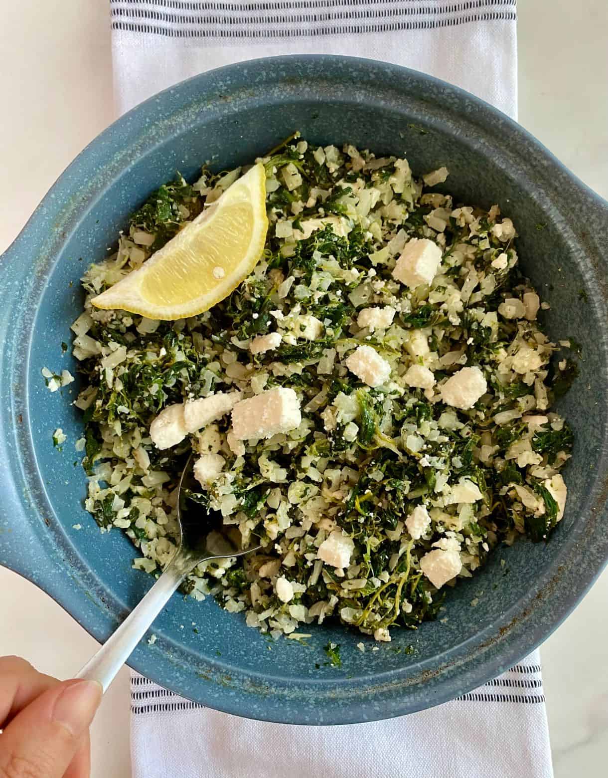 A dish with cooked Mediterranean Cauliflower Rice and a wedge of lemon.