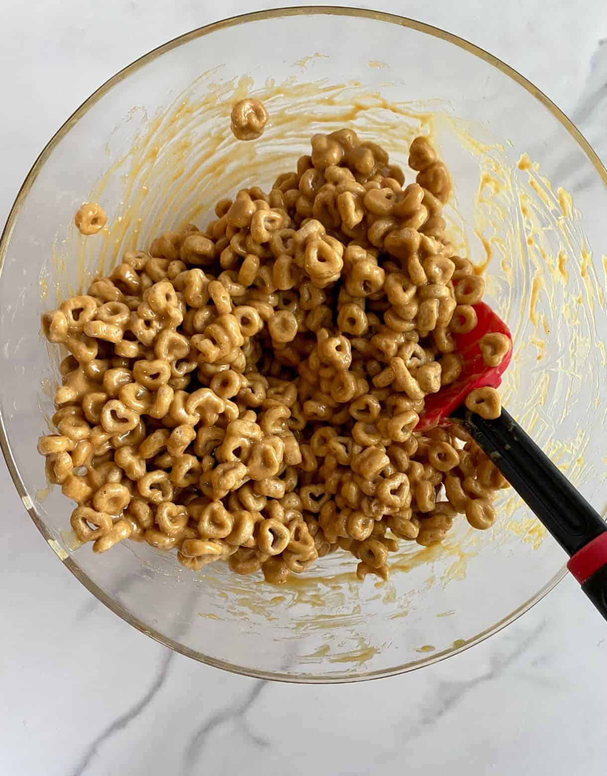A bowl of Cheerios coated and stirred with a peanut butter honey mixture.