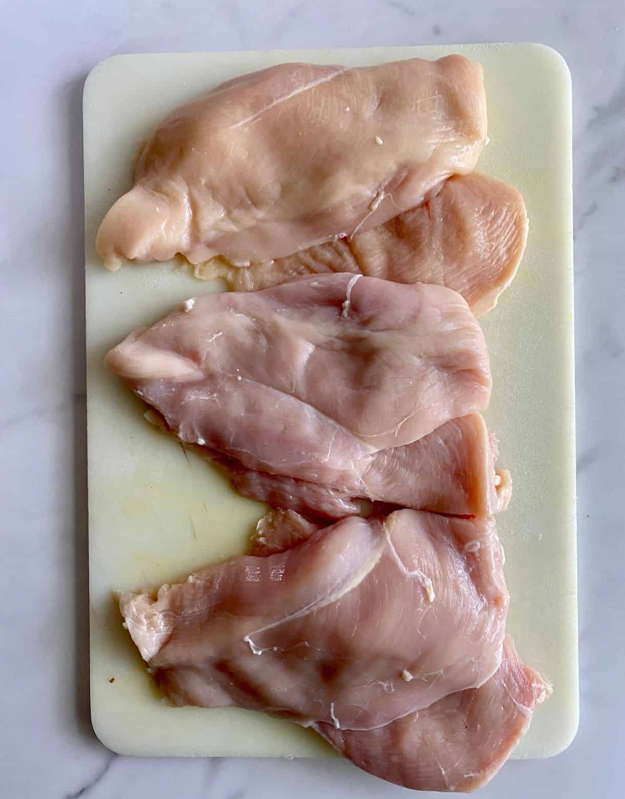 A cutting board with chicken breasts sliced into cutlets.