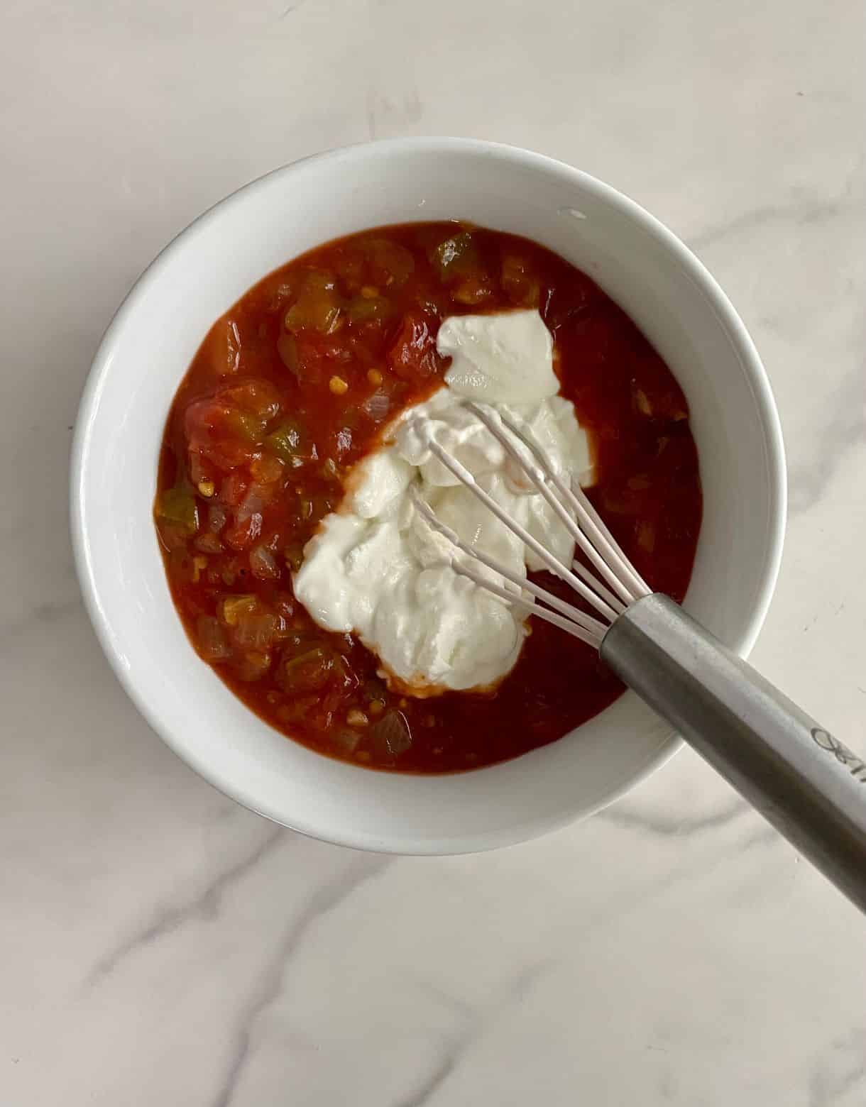 A bowl with salsa, sour cream and a whisk.