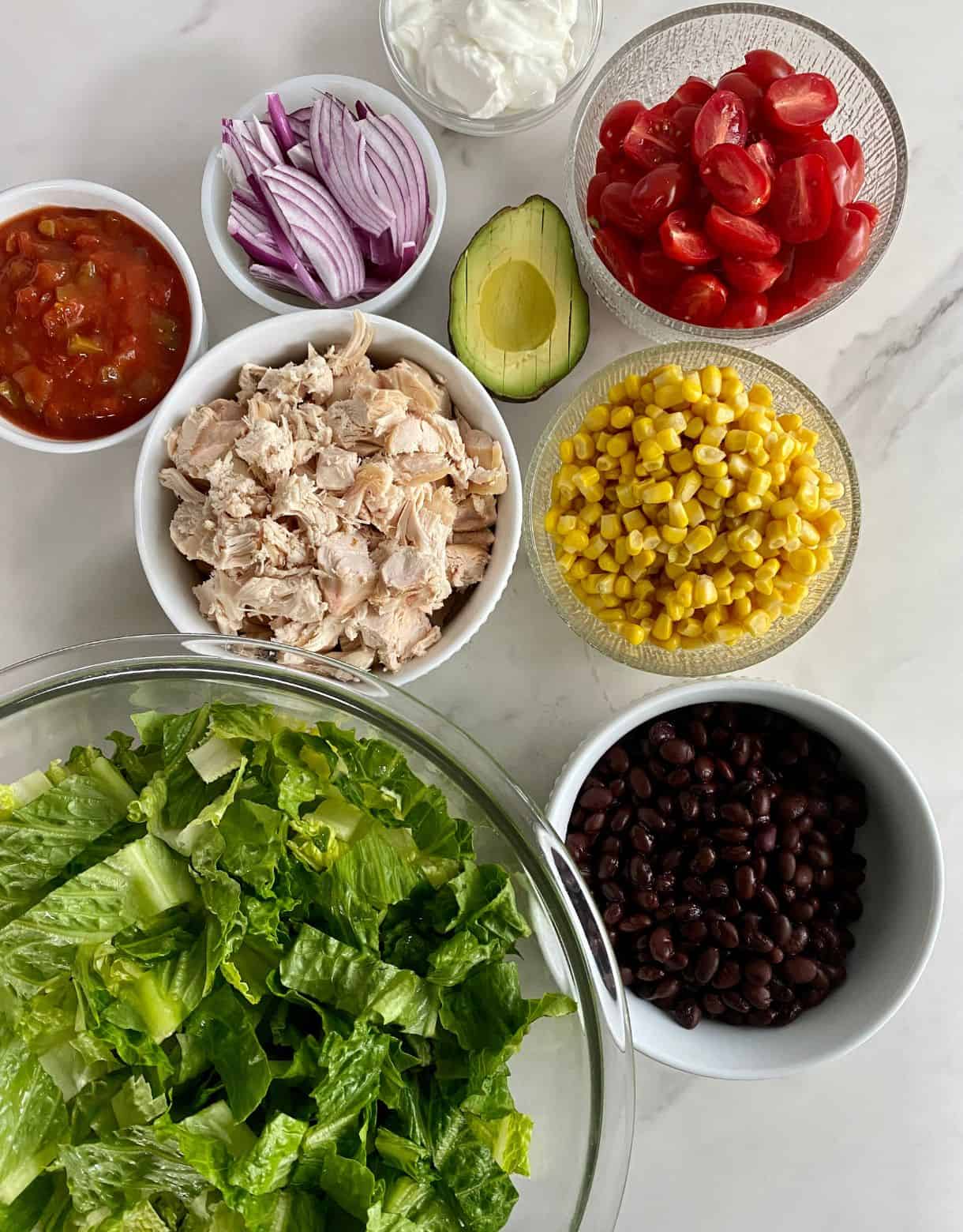 Sliced romaine lettuce, black beans, corn, chopped cooked chicken, salsa, sour cream, sliced avocado, halved grape tomatoes and sliced red onion.