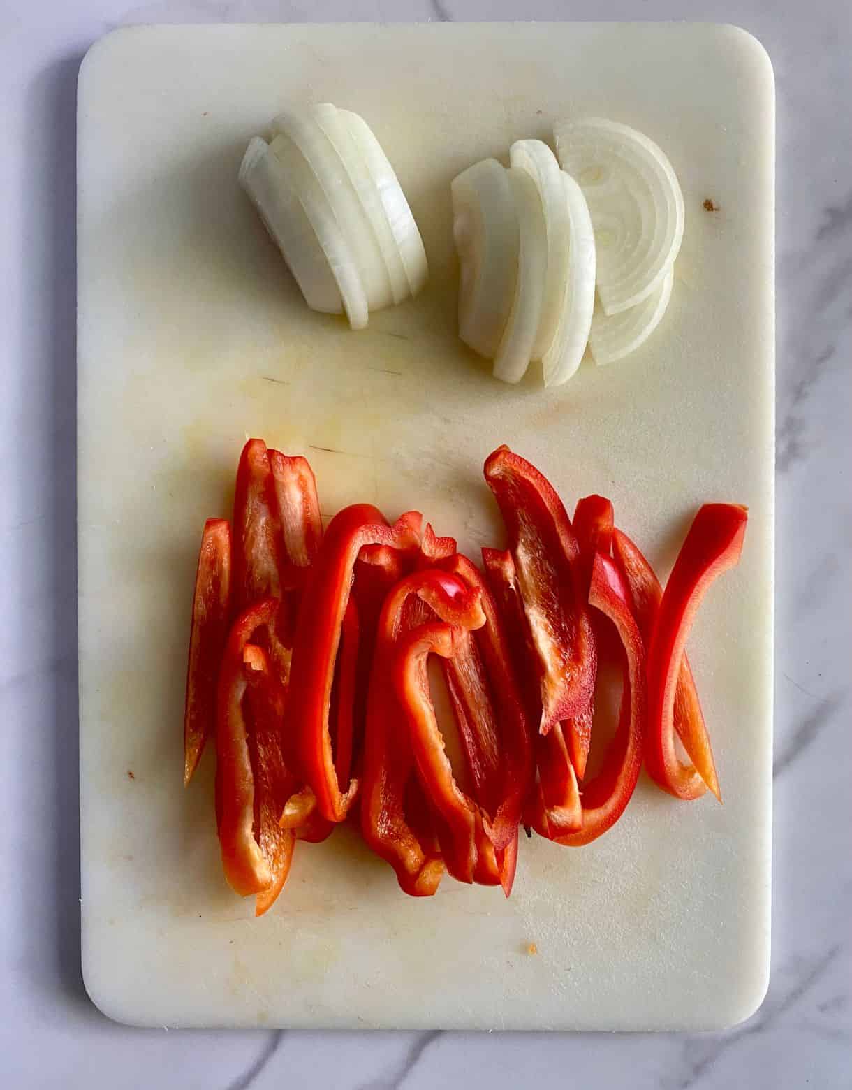 A cutting board with sliced onion and red bell pepper.