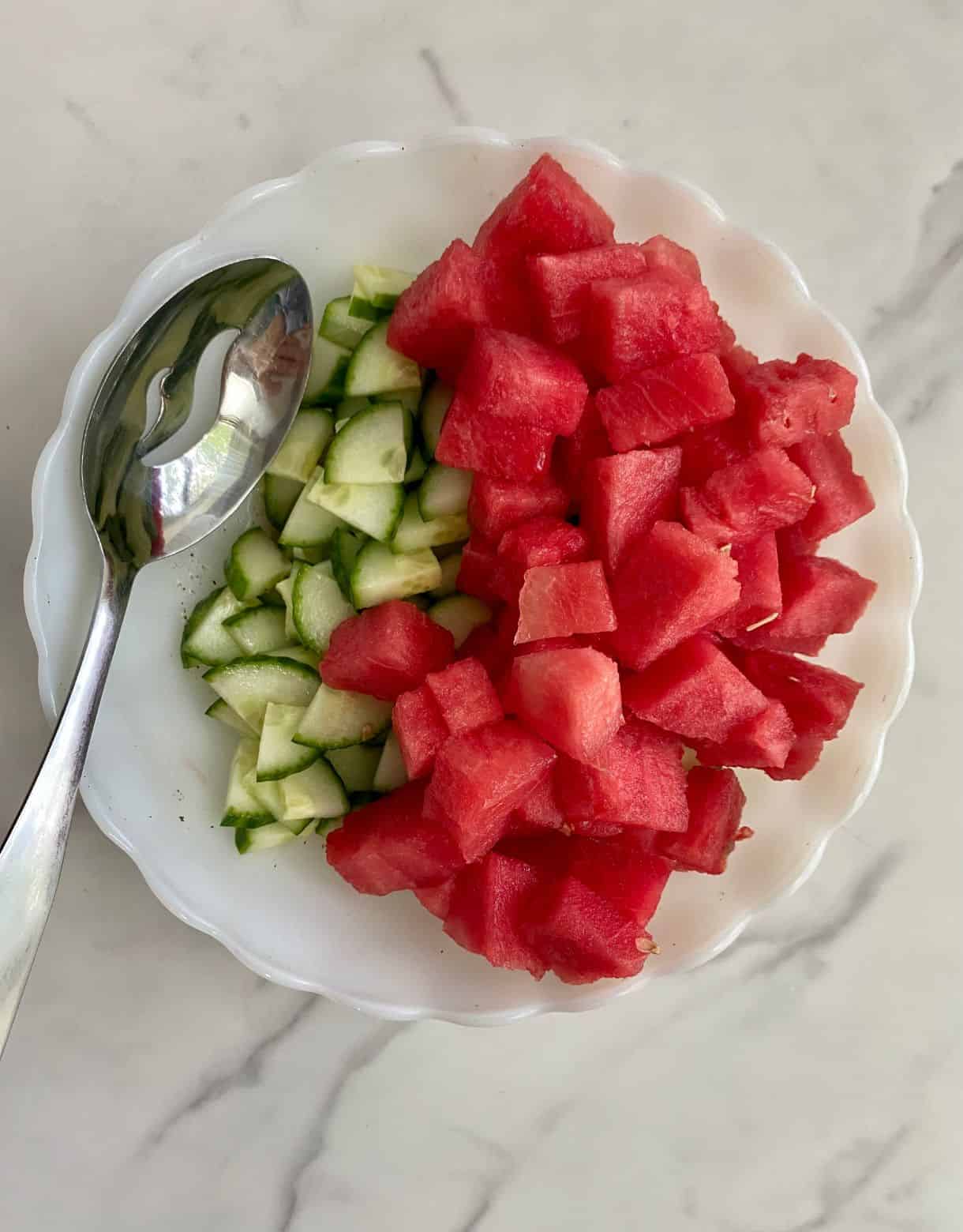 A bowl with chopped watermelon and diced cucumber in it but not stirred together.
