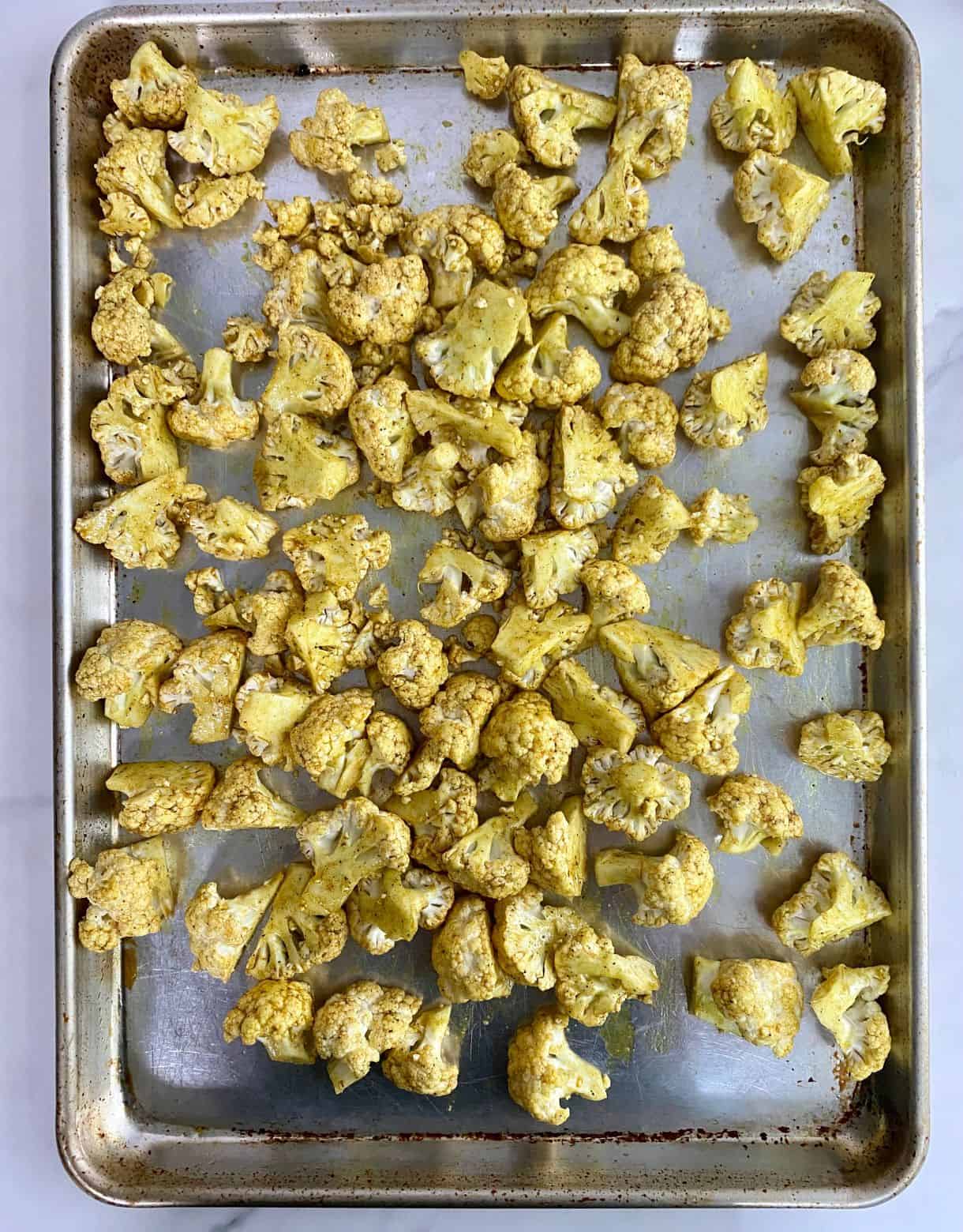 A sheet pan of raw seasoned cauliflower ready to go in the oven.