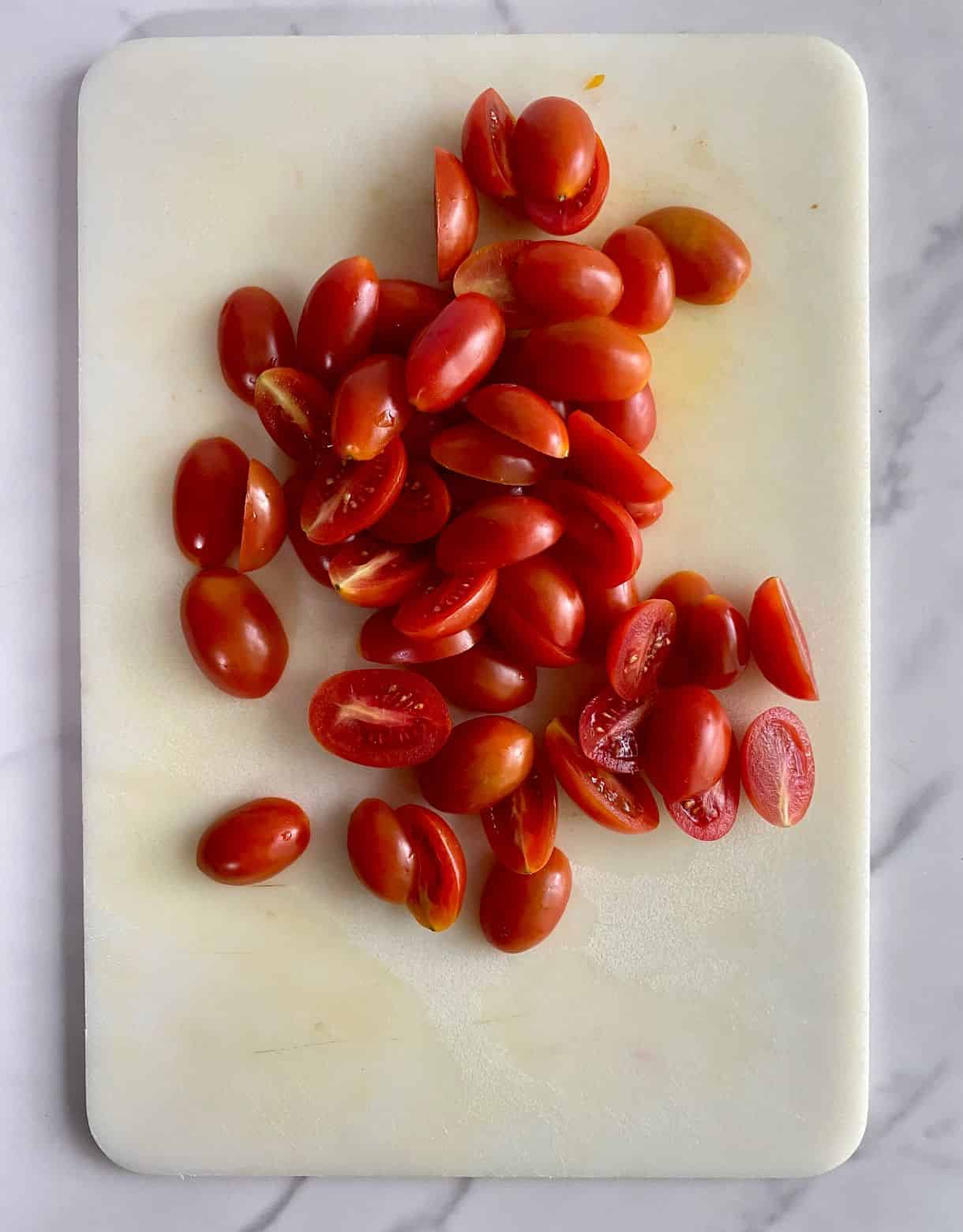 A cutting board with sliced grape tomatoes.