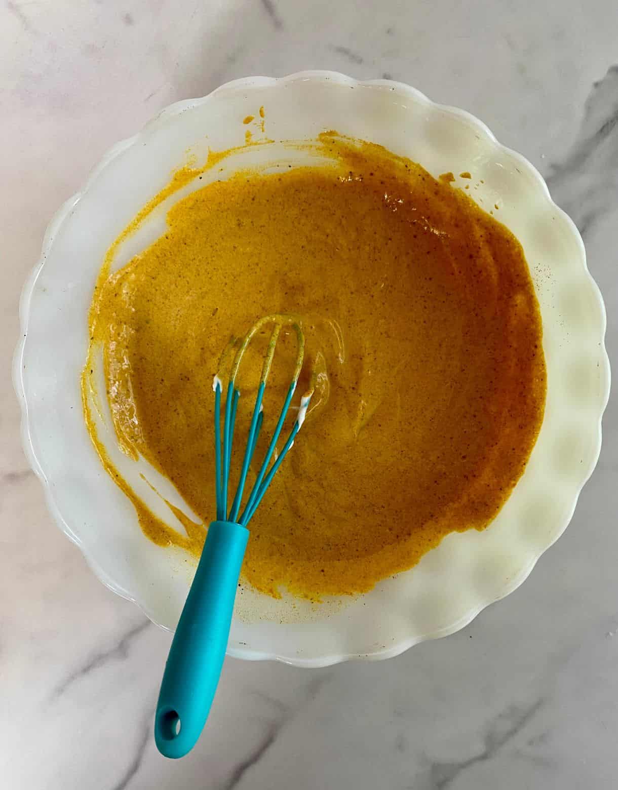 A bow of curry dressing with a whisk.