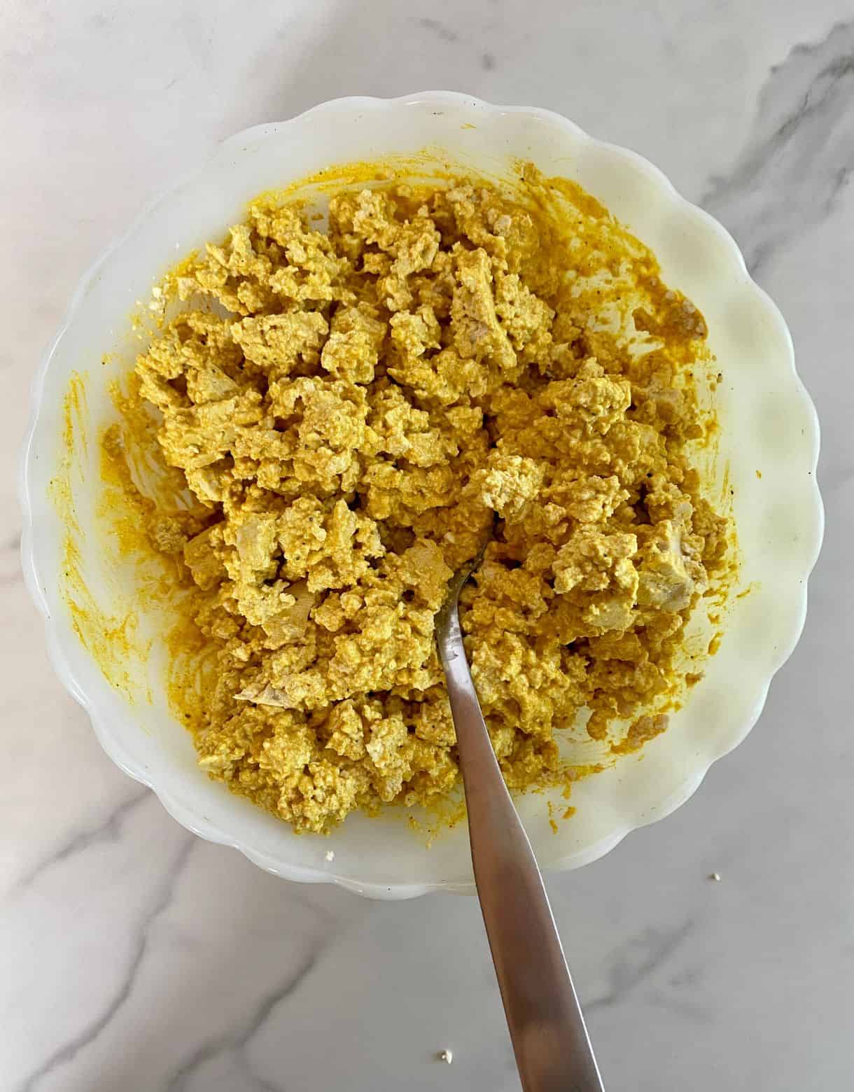 A bowl of crumbled tofu mixed with curry dressing.
