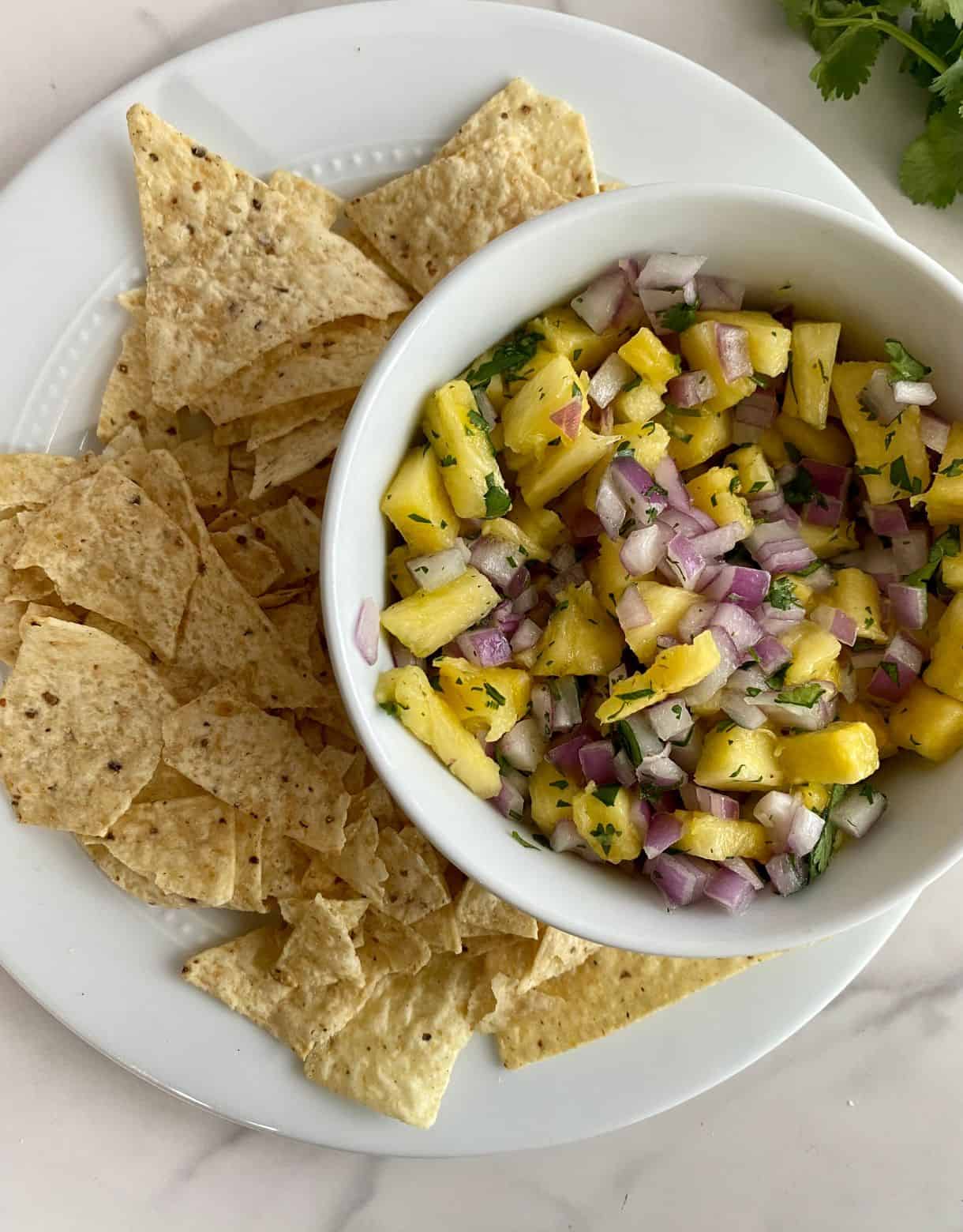 A bowl of Pineapple Pico de Gallo on a plate full of tortilla chips.