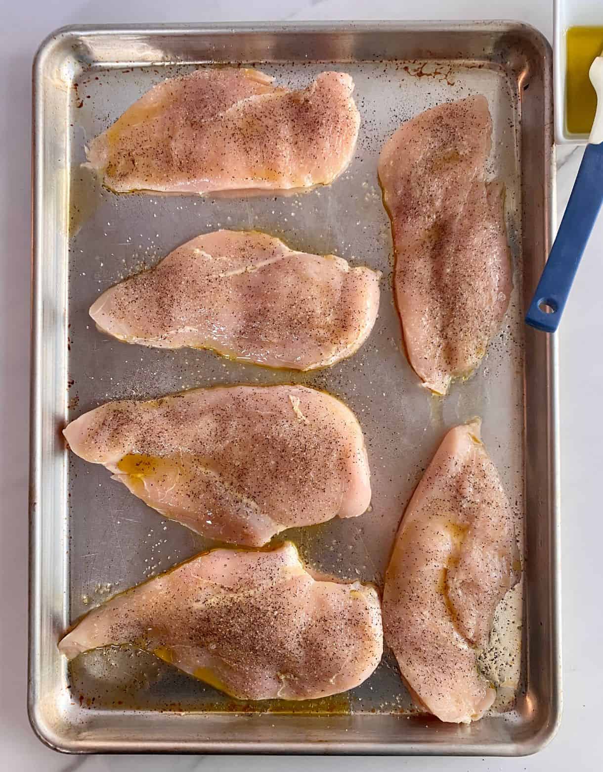 A sheet pan with raw seasoned chicken cutlets.
