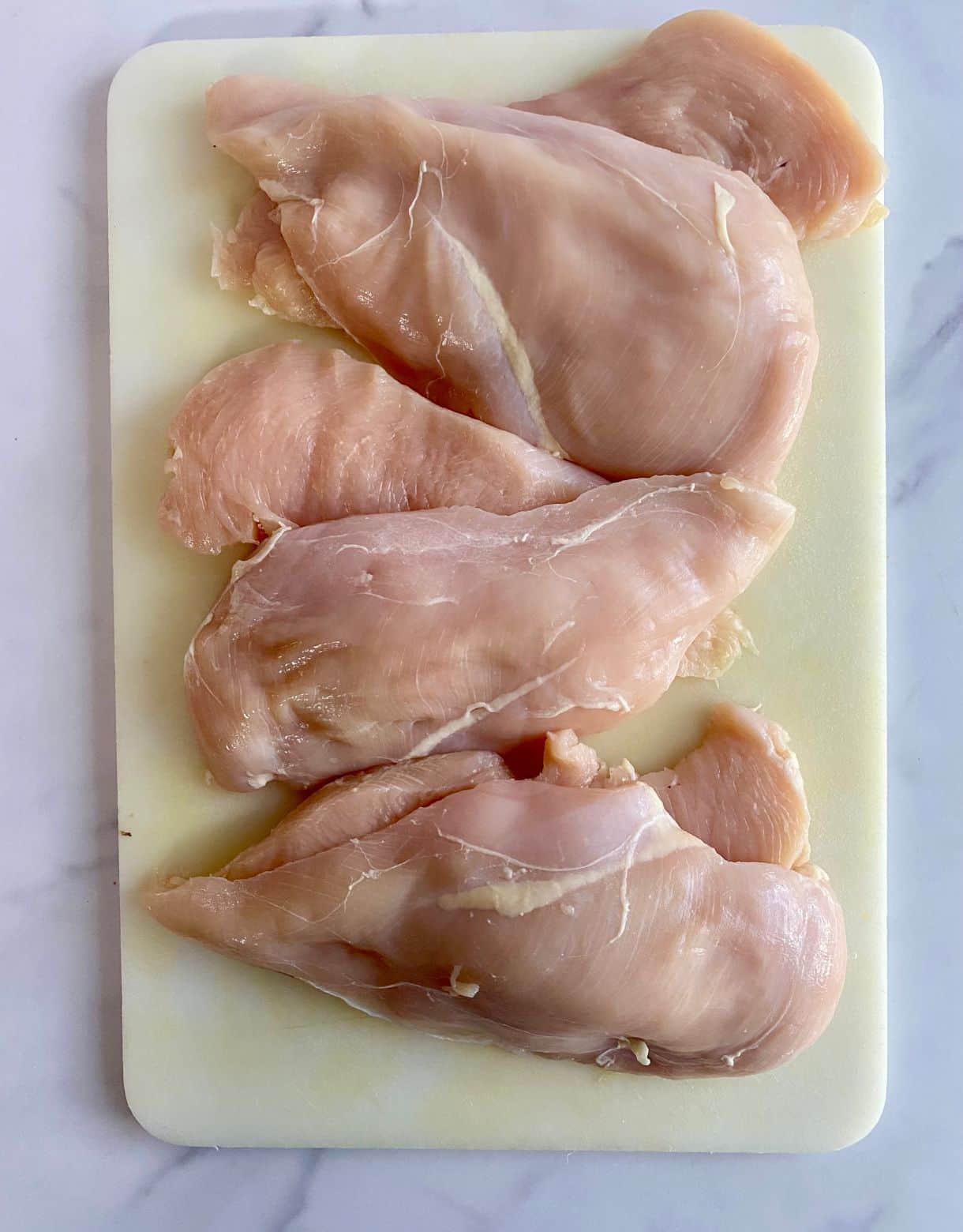 A cutting board with chicken breasts sliced into cutlets.