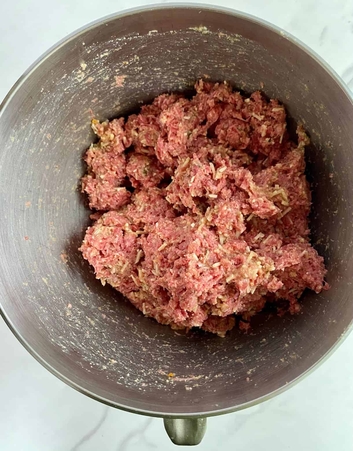 A bowl of raw ground beef mixed with milk, eggs, bread crumbs, parmesan cheese and spices.