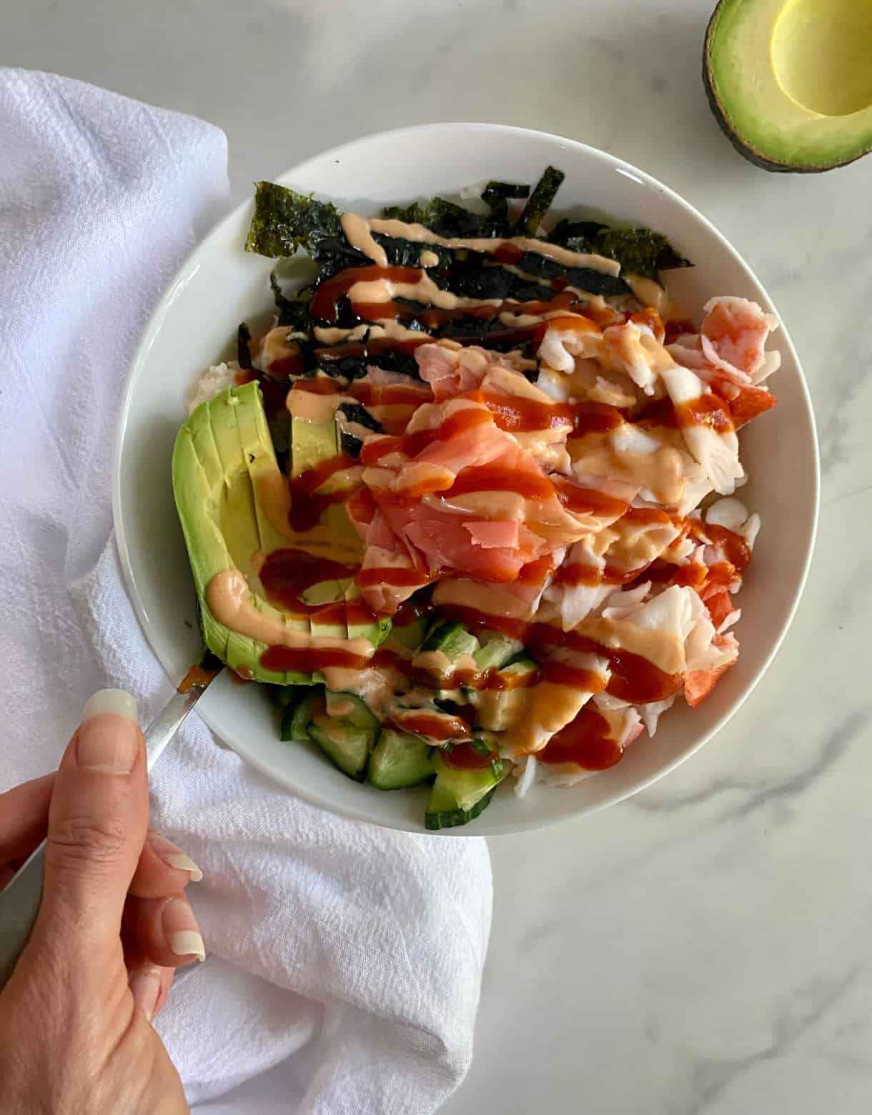 A Deconstructed Sushi Bowl with cauliflower rice, crab, avocado, cucumbers, seaweed, pickled ginger and sriracha mayo.