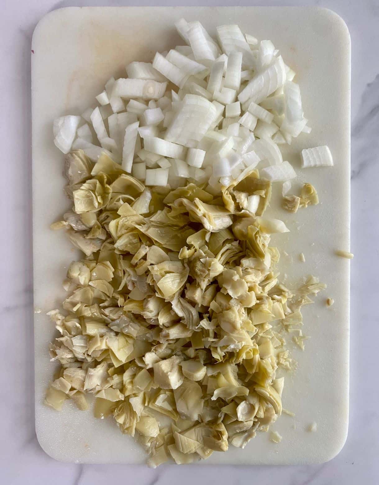 A cutting board with diced onion and artichoke hearts.