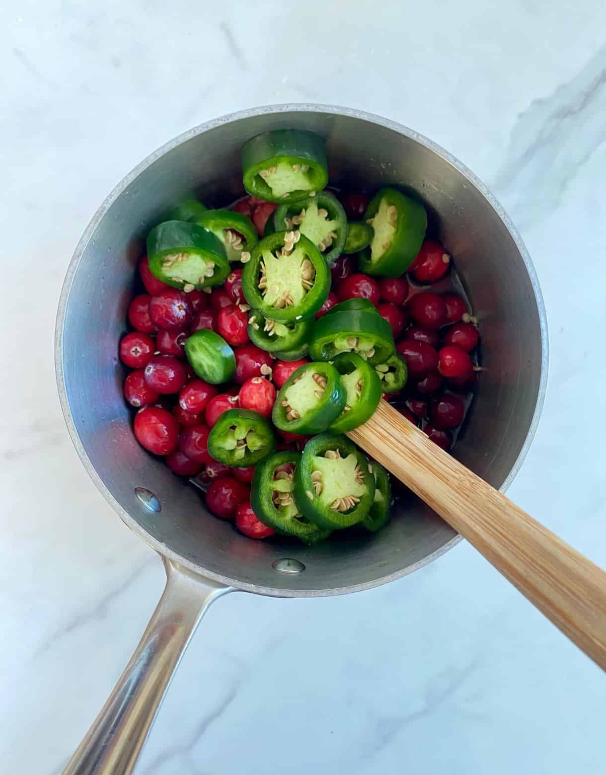 A small pot with fresh cranberries and sliced fresh jalapenos added but not yet cooked or stirred.