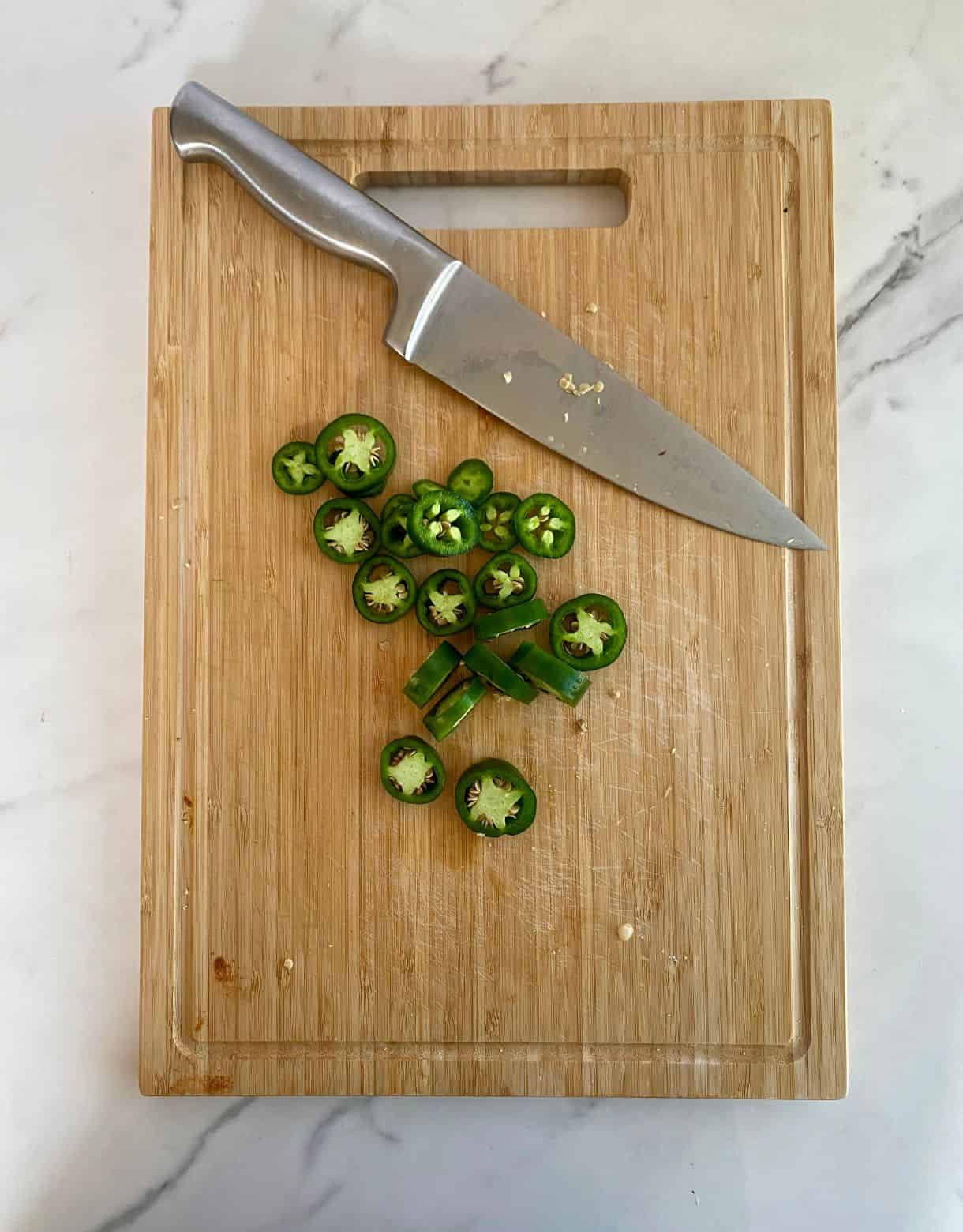 A cutting board with a knife and a sliced jalapeno.